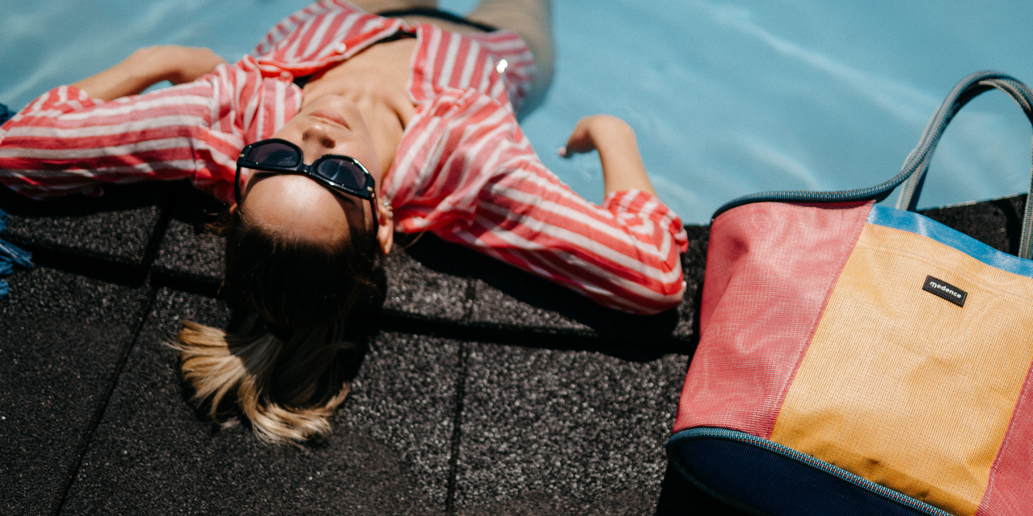 Person lying by the pool next to a colorful bag 